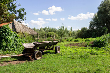 Cart on green meadow. Old barn roof and wooden fences.