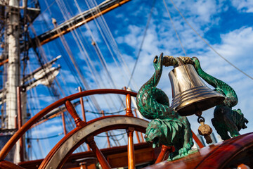 Clipper sailboat nautical equipment. Polished ship bell with bronze figurehead on wooden deck.