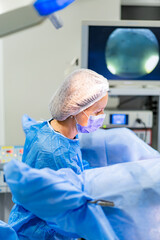 Surgeon at work in OR. A medical professional in blue scrubs and a mask focuses during surgery in a...