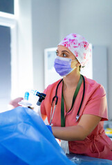 Surgeon prepping equipment. A nurse in pink scrubs and a floral cap readies surgical tools in a...