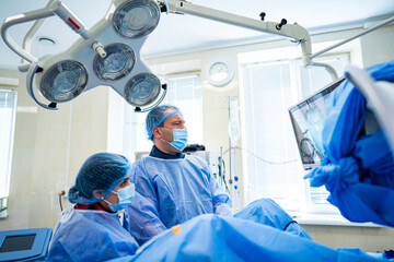 Surgeons operating in hospital. Medical professionals in blue scrubs and masks focus intently on a...
