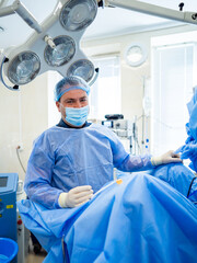 Surgeon preps for surgery. A surgeon in blue scrubs and mask stands ready in an operating room,...