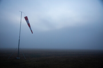 An anemoscope, consisting of a support pole and a windsock, immersed in the morning fog, on the plain, Castelluccio di Norcia, Sibillini Mountains, Umbria, Italy