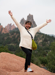 Senior citizen female hiker expressing joy while standing on the top of a rocky outcropping.