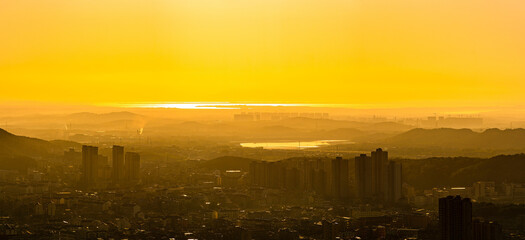 The sun shines brightly over the city skyline and a vast lake, casting a warm golden glow as it...