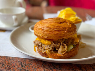 Croissant sandwich with meat and melted cheese served on a plate in a cozy cafe. Gastronomy, lifestyle, and casual dining experience with comfort and indulgence.