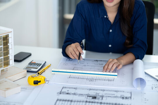 Asian female architect meticulously design building blueprints develop projects professional office workspace engineering construction plan detailed drafting measurement scale ruler desk