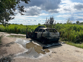 Burnt abandoned car on rural dirt road near green field