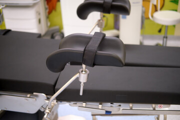 Detailed view of a black padded medical stirrup with strap attached to an examination or surgical table in a hospital setting.