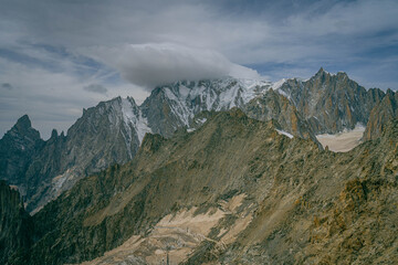 Expansive mountain ridge in the Alps with sharp rock faces and patches of snow beneath dark storm clouds creating powerful alpine view