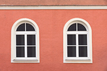 two arched white lattice windows at rough red painted house facade
