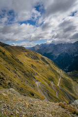 Fototapeta premium Stelvio Pass serpentine road weaving up alpine mountainside with panoramic view of peaks and valleys under shifting clouds dramatic scenery