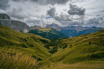 Dolomites alpine valley with grassy slopes, rocky cliffs and high peaks under storm clouds creating dramatic mountain landscape scene