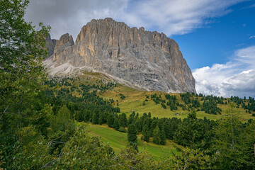 Dolomites mountain view of Langkofel Group with grassy meadow and rocky cliffs under storm clouds creating dramatic alpine scenery