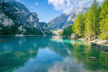 Pragser Wildsee Dolomites lake with emerald water, forested shoreline and high cliffs under clear summer sky panoramic alpine scene