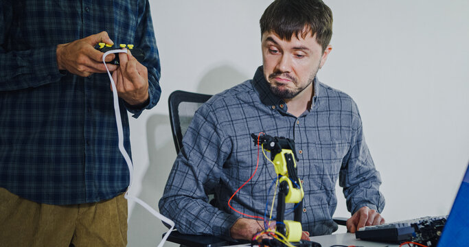 Team adult male engineer collaborate on robotic hand project using AI code solutions machine learning at tech workspace. Artificial intelligence interface, collaboration support prototype development.