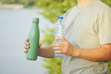 Eco lifestyle concept: man holding reusable metal water bottle and plastic bottle outdoors. Contrast between sustainable choice and disposable waste, symbolizing zero waste, recycling, mindful habits