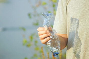 A man standing against the backdrop of green bushes and a river and crushing a plastic bottle in his hand. Urgent issue of plastic pollution. Symbol of eco-conscious behavior and sustainable living