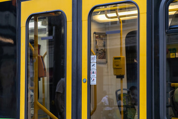 Modern yellow and black public transport doors featuring clear safety signs, interior grab bars, ticket validator, and passenger reflections, enabling efficient urban transit