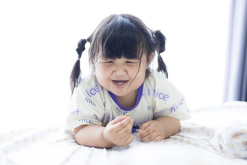 Fototapeta premium A cute little Asian girl is smiling happily on the bed,Newborn baby girl laughing happily, cute smile of little asian child and childhood concept.