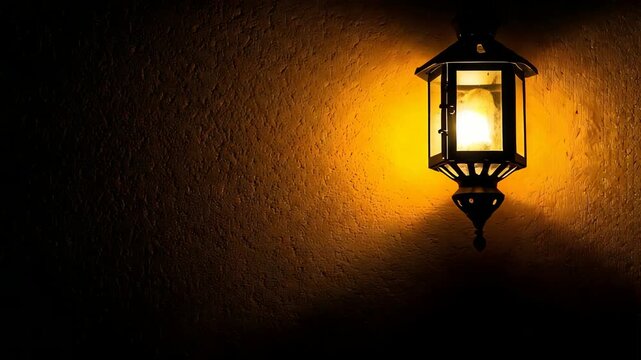 Close-up 4k video of a vintage, ornate lantern emitting warm light against a dark textured wall, creating a moody, atmospheric scene.