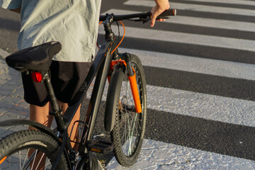 Fototapeta premium Boy on a bicycle looking away from the camera, standing at a pedestrian crossing, a concept of urban life, safety, and a healthy lifestyle.