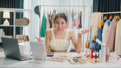 Young beautiful Asia lady blogger looking at camera recording swatch apply eyeshadow palette on skin show review to follower product vlog video live streaming at home. Business online media concept.