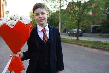 Young Boy in a Suit Holding a Bouquet of Flowers Outdoors, Smiling on a Street