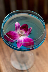 Flower-adorned colorful drink. A vibrant cocktail features a purple flower floating atop, showcased in a stylish blue glass.