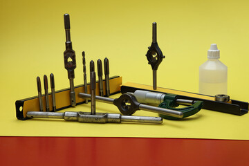 Obraz premium Still life taps and dies. Close-up with used taps, dies, holders, drill, lubricant and micrometer. Photo with maximum depth of field on a yellow background.