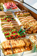 Tasty buffet on a sunny day. A vibrant selection of sandwiches, salads, and desserts laid out on a table, enjoyed on a sunny day by the water.