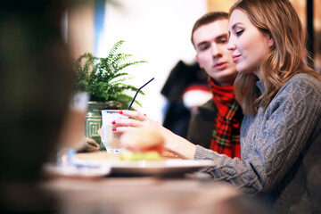 Couple in a restaurant or diner eating a hamburger and chicken wings flirting the while, shot with available light, very selective focus