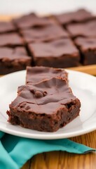 Deliciously rich chocolate frosted brownies stacked on a white plate with more in the background