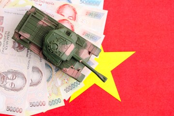Vietnamese dong currency money bills and toy tank on flag. The concept of army funds and weapons sales