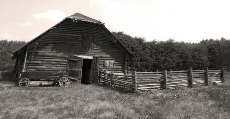 Old wooden barn surrounded by greenery and a rustic fence on a sunny day in the countryside
