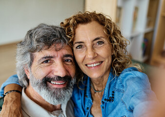 Portrait of a happy senior couple taking a selfie embracing hugging and having fun at home