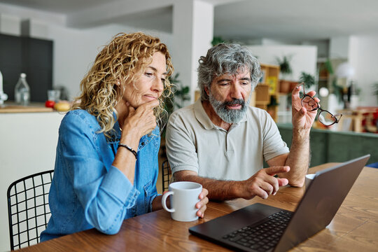Portrait of a lovely senior mature couple using a laptop together and having fun drinking coffee or tea sitting at a table at home
