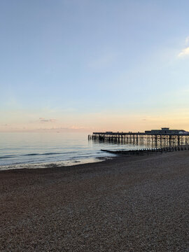 Scenic Coastal Pier at Sunset with Calm Sea, Pebble Beach, Gentle Waves, and Clear Evening Sky