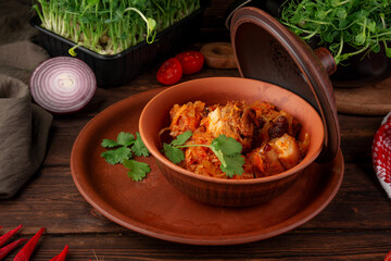Hearty traditional stewed meat with cabbage carrots and spices served in clay pot garnished with fresh parsley on wooden table