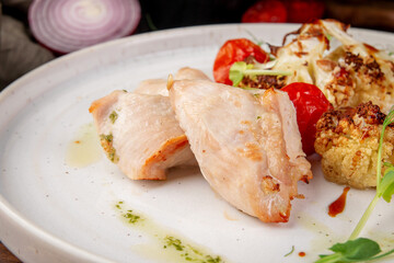Juicy baked turkey fillet served with roasted cauliflower, cherry tomatoes and herbs on white plate in rustic food styling
