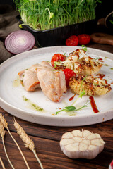 Juicy baked turkey fillet served with roasted cauliflower, cherry tomatoes and herbs on white plate in rustic food styling