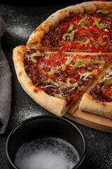 Freshly baked homemade pizza with meat, tomato, bell pepper, pickles and grated cheese sliced on wooden board rustic background