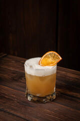 Citrus yellow cocktail with airy foam and dried orange garnish served in short glass on rustic wooden table