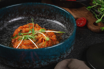 Traditional stewed cabbage in tomato sauce with fresh herbs served in dark ceramic bowl on rustic table