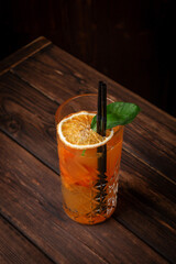 Refreshing highball cocktail with orange juice, basil, ice cubes and dried orange slice in tall crystal glass on wooden table