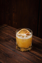 Classic whiskey sour cocktail with ice cubes and dried orange slice served in lowball glass on rustic wooden table