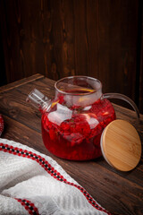 Hot berry fruit tea with fresh raspberry, lemon slices and herbs served in transparent glass teapot on rustic wooden table