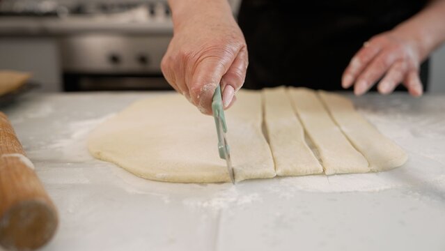 Baker cutting dough into strips in kitchen