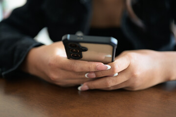Close-up of woman hands texting and chatting using mobile phone indoors in coffee shop restaurant