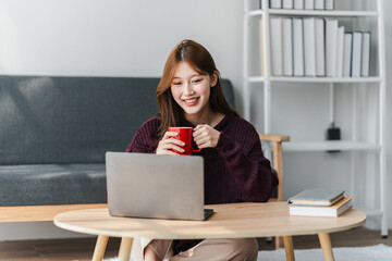 Young Asian Woman Working on Laptop with Coffee at Home Enjoying Online Work and Relaxing in Cozy...